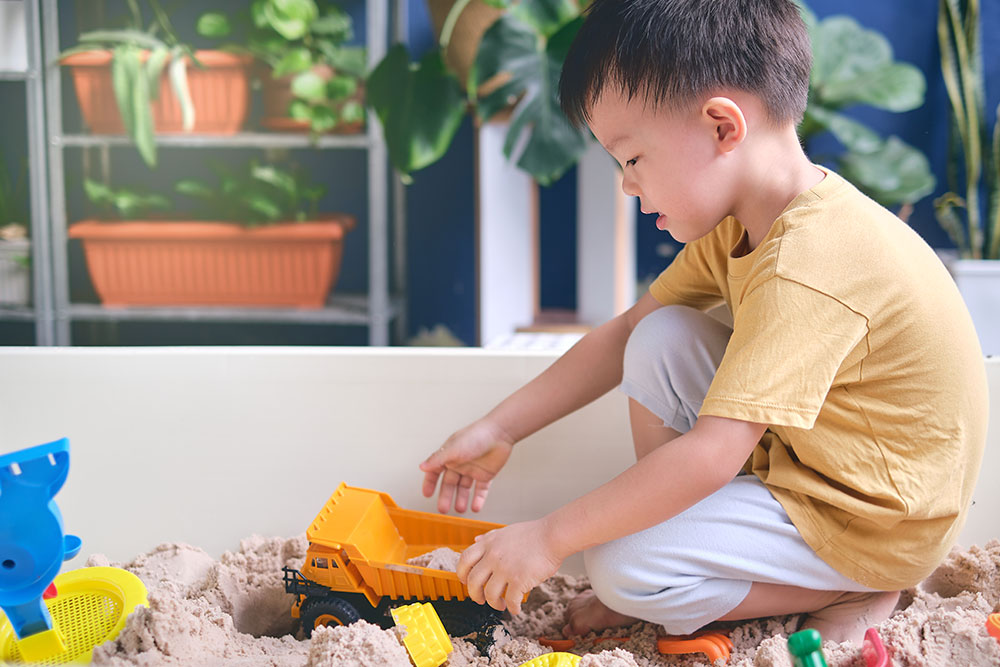 "Child's Kinetic Sand Exploration: Building with Toy Construction Vehicles"